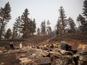 Robert Hugh, left, and his partner Michelle Maisonneuve, back, look over the remains of their home that was destroyed by the White Rock Lake wildfire in Monte Lake, east of Kamloops, B.C., Saturday, Aug. 14, 2021.