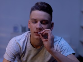 Male teenager smoking joint at home.