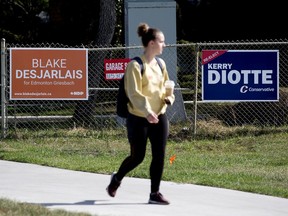 A pedestrian makes their way past signs for Edmonton Griesbach Federal election candidates Blake Desjarlais and Kerry Diotte, near 70 Street and 112 Avenue in Edmonton, Tuesday Sept. 7, 2021. Photo by David Bloom