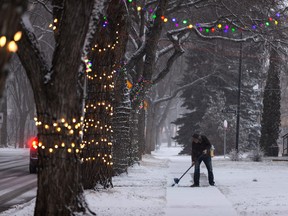 Chris Maximchuk clears a sidewalk next to trees covered in Christmas lights as snow falls on 74 Street near 109 Avenue during the first big snowstorm of the season in Edmonton, on Monday, Nov. 15, 2021. Photo by Ian Kucerak