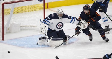 Edmonton Oilers Zach Hyman (18) is held back by Winnipeg Jets Connor Hellebuyck (37) during second period NHL action on Thursday, Nov. 18, 2021 in Edmonton.
