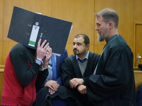 Iraqi Taha Al-J. hides behind a folder speaking to his lawyers Serkan Alkan (C) und Martin Heising (R) before the judgment is pronounced in the Frankfurt Higher Regional Court on November 30, 2021 in Frankfurt an Main, Germany.