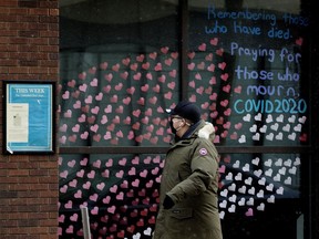 A pedestrian wearing a mask to protect against COVID-19 walks past hundreds of paper hearts posted on the windows of All Saints' Anglican Cathedral, 10035 103 St., in memory of people lost to COVID-19, in Edmonton Thursday Jan. 21, 2021. The paper hearts stretch around the front of the building.