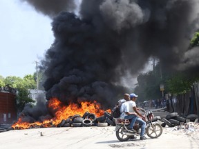 People ride on a motorcycle near a burning barricade as Haitians mount a nationwide strike to protest a growing wave of kidnappings, days after the abduction of a group of missionaries, in Port-au-Prince, in Haiti October 18, 2021.
