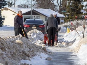 Neighbours Dana Sydor, Isa Khurshed, and Nizam Khurshed clear the windrows from in font of their homes shortly after a grader had created them on Wednesday, Jan. 12, 2022 in north Edmonton.