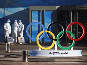 Workers in PPE stand next to the Olympic rings inside the closed loop area near the National Stadium, or the Bird's Nest, where the opening and closing ceremonies of Beijing 2022 Winter Olympics will be held, in Beijing, China, Thursday, Dec. 30, 2021.