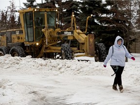 A pedestrian walks past City of Edmonton crews removing snow from the roads in Edmonton's Griesbach neighbourhood, in January.
