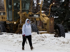 A pedestrian walks past City of Edmonton crews removing snow from the roads in Edmonton's Griesbach neighbourhood on Jan. 21, 2022.