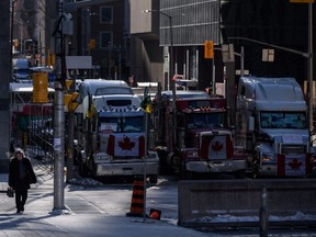 A woman walks near vehicles blocking a road during a protest by truck drivers over pandemic health rules and the Trudeau government, outside Parliament Hill in Ottawa on Monday, Feb. 14, 2022.