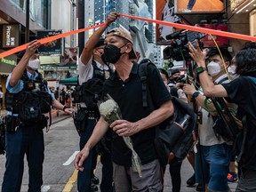 A man holding a flower bouquet is escorted by police officers at Causeway Bay district near Victoria Park, the traditional site of the annual Tiananmen candlelight vigil, on June 4, 2022 in Hong Kong.