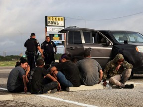 Asylum seeking migrants from Central America sit next to a vehicle that was stopped by police after crossing the Rio Grande into Eagle Pass, Texas, from Mexico along U.S. Route 90, in Hondo, Texas, Wednesday, June 1, 2022.