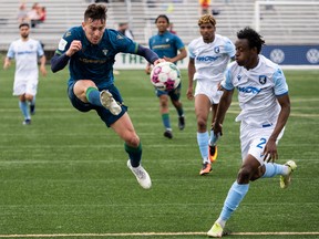 FC Edmonton's Bicou Bissainte (25) watches an airbourne York United FC's Mateo Hernández (10) kick the ball during first half Canadian Premier League action at Clarke Stadium in Edmonton on July 1, 2022.