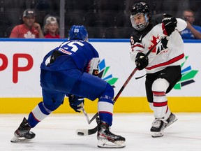 Kanadský tím Conor Bedard (16) udrie cez nohy slovenského tímu Simona Groscha (25) počas druhej tretiny počas juniorských majstrovstiev sveta v hokeji na Rogers Place v Edmontone vo štvrtok 11. augusta 2022.