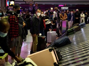 Airline passengers wearing face masks wait to collect bags from a baggage carousel at the Harry Reid International Airport (LAS) on January 2, 2022 in Las Vegas, California.(Photo by PATRICK T. FALLON/AFP via Getty Images)