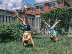 Two young girls turn cartwheels in a fenced yard
