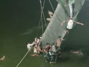 People cling on to the collapsed suspension bridge in Morbi, India Oct. 30, 2022 in this screen grab obtained from a video.