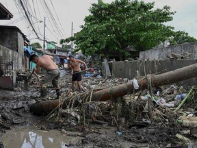 Men clean the debris along a debris-covered street in Noveleta, Cavite province on Oct. 30, 2022, a day after Tropical Storm Nalgae hit.
