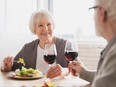 Happy senior couple drinking wine, eating salad at home.