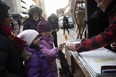 Pranavi Bhatt, 9, gets some maple syrup candy as Meera Bhatt, 7, looks on during the Downtown Holiday Light Up in Edmonton, Alta. on Dec. 3, 2022.