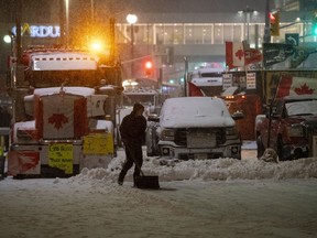A protester shovels snow in front of parked semi-trailer and pickup trucks on Rideau Street, on the 21st day of a protest against COVID-19 measures that has grown into a broader anti-government protest, in Ottawa, Feb. 17, 2022. The Defence Department's top official says he told the military to prepare to intervene as "Freedom Convoy" protests gridlocked downtown Ottawa and several border crossings with the U.S. earlier this year.