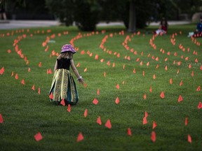Margot King, 4, touches an orange flag, representing children who died while attending Indian Residential Schools in Canada, placed in the grass at Major's Hill Park in Ottawa, July 1, 2021.