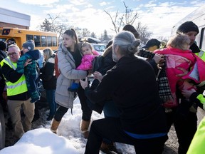 Parents and their children are loaded onto a warming bus as they wait for news after a bus crashed into a daycare centre in Laval Feb. 8, 2023.