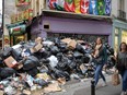 Pedestrians walk past full waste bins in Paris' 5th district as rubbish collectors strike against pension reforms, leaving many streets in the capital piled with stinking waste on March 17, 2023.