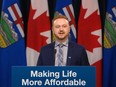 Justice Minister Mickey Amery stands behind a podium against a backdrop of Canadian and Alberta flags