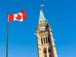 Close up of peace tower (parliament building) with a big canadian flag over blue sky in Ottawa.