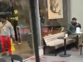 Screen shot of man sitting on Starbucks patio and drinking coffee as man is stabbed in front of him and suspect in red pants went back inside.