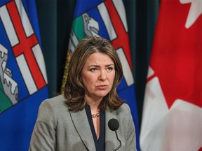 Danielle Smith speaks into a microphone on a platform with Alberta and Canada flags in the background.