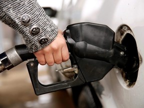 A hand holds a gas pump nozzle as it fuels a car.
