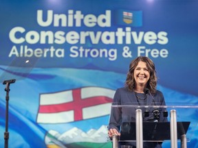 Danielle Smith stands behind a podium with a United Conservatives, Alberta Strong & Free ceiling to floor banner in the background