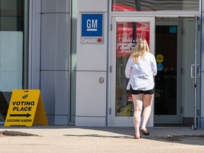 A woman enters an office building. A yellow temporary sign next to the door indicates it is a voting location.