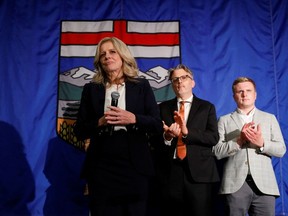 Rachel Notley stands on a stage with supporters and a giant Alberta flag in the background