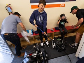Two children aged 11 and 12 are being outfitted by two adults with hockey equipment in a hockey rink changing room.