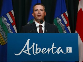 Nate Horner, Alberta's Mnister of Finance , stands behind a podium in front of a backdrop of Canadian and Alberta flags