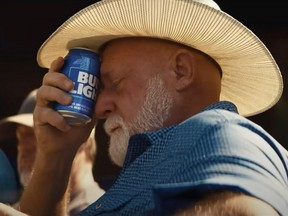 Man in cowboy hat holding Bud Light can to forehead.