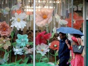 Pedestrians make their way through the rain past a flower window display at Maven and Grace Hardwares, 9609 82 Ave., in Edmonton Sunday, June 18, 2023.