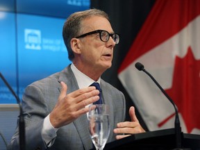 Tiff Macklem, Governor of the Bank of Canada, gestures with his right hand while sitting at a table and speaking into a microphone.