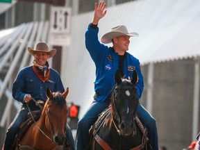 Astronaut Jeremy Hanson, wearing his NASA jacket and a white hat, waves to the crowd as he leads the Stampede parade on the back of a black horse
