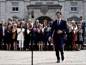 Members of the federal cabinet applaud as Prime Minister Justin Trudeau walks up to a microphone stand.