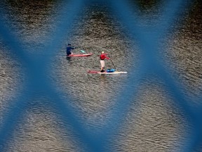 Stand-up paddle boarders are framed by a pedestrian railing on the Dawson Bridge, as they head down the North Saskatchewan River in Edmonton Friday July 28, 2023.