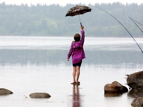 Lily Rux, 7, balances on a rock while fishing in the rain with her grandmother Jackie Fryk (just out of frame) along the North Saskatchewan River under the Quesnell Bridge in Edmonton, Tuesday Aug. 8, 2023.