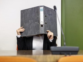 A defendant who allegedly joined the terrorist militia Islamic State (IS) in Iraq, holds a file folder in front of her face in the courtroom of the Higher Regional Court, as she sits next to her lawyer Tarig Elobied, in Munich, Germany, Tuesday Aug. 29, 2023. The Munich court sentenced the German woman to 14 years in prison on charges that, as a member of the Islamic State group in Iraq, she allowed a 5-year-old Yazidi girl she and her husband kept as a slave to die of thirst in the sun. The verdict overturned an earlier prison sentence of ten years.