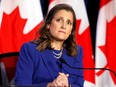 Federal finance minister Chrystia Freeland sits behind a microphone against a backdrop of Canadian flags