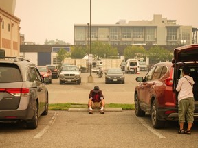 A man sits in the parking lot outside an evacuation centre for those forced from their homes due to wildfires in Kelowna on Saturday.