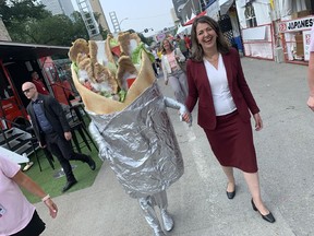 Alberta Premier Danielle Smith walks among the tents at Taste of Edmonton Thursday, July 20, 2023, accompanied by someone wearing a donair costume similar to the one currently being auctioned by the Alberta government on its surplus auction website.
