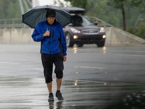 A pedestrian walks in the rain near the Walterdale Bridge on Wednesday, July 26, 2023 in Edmonton.