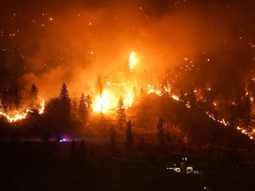 The McDougall Creek wildfire burns on the mountainside above a lakefront home, in West Kelowna, B.C., on Friday, Aug. 18, 2023.
